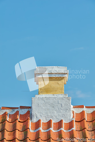 Image of Brick chimney designed on slate roof of house building outside against blue sky background. Construction of exterior architecture of escape chute built on rooftop for fireplace smoke and heat