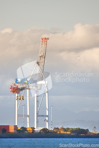 Image of A crane and shipping containers in a shipyard surrounded by the ocean. Industrial hoisting crane in a logistics or cargo harbor at a seaport for the transportation of liquid materials