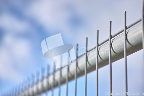 Image of Closeup of a new metal fence against a cloudy blue sky. Safety and security to protect your home and property. Sharp spikes to keep people out. Constructing a fence or cage. Danger keep out