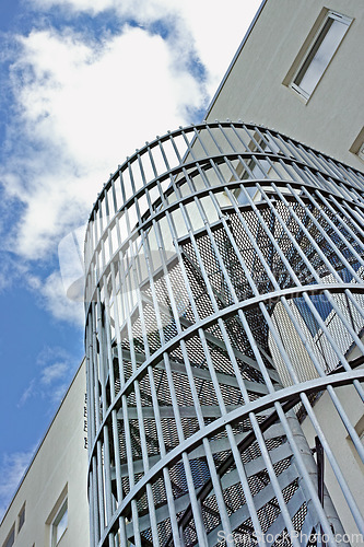 Image of A spiral staircase on the outside of a building. Grey steel spiral stairs built on the side of modern industrial office building. Low angle of a metal circular fire escape staircase with railings