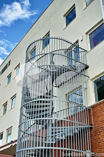 Image of A spiral staircase running down the side of a building. Emergency exit fire escape. Backyard escape stairs. Caged emergency ladder for the safety of the residents in case of a fire or fire drill