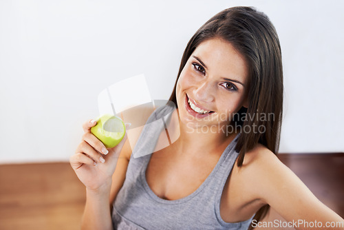 Image of Portrait, smile and apple with a woman eating fruit for health, diet or nutrition in the kitchen of her home. Food, nutritionist and a happy young model in a house for organic wellness or weight loss