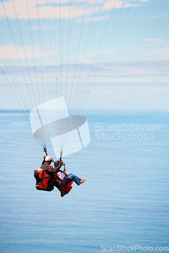 Image of Sky, ocean and air with a couple in a parachute together for travel, freedom or adventure. Sea, summer or nature with a man and woman flying over the water while bonding on holiday or vacation