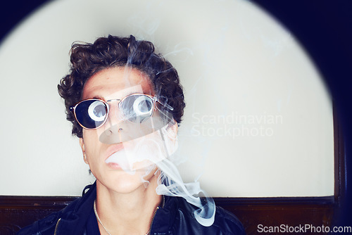 Image of Portrait of man smoking, sunglasses and grunge fashion with rockstar attitude on white background in spotlight. Cool punk style, creative and smoke, confident face of handsome male model in studio.