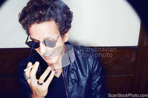 Image of Man with cigarette, rock fashion and smile with rockstar attitude on white background in spotlight. Cool punk style, grunge and smoking, confident and happy male model in studio with sunglasses.