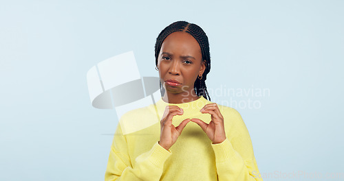 Image of Woman, portrait and hands of broken heart in studio for sad breakup, depression and lonely emotion on blue background. Unhappy african model show heartbreak emoji for divorce, trauma and pain of love