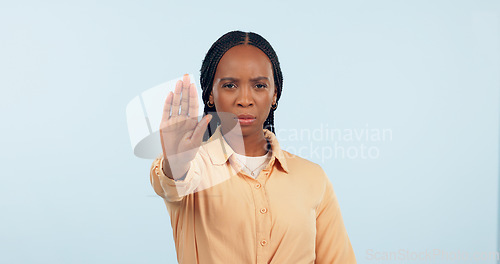 Image of Serious, stop sign and portrait of black woman in a studio for activism, protest and human rights. Upset, mad and young African female person with open palm hand gesture isolated by blue background.