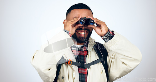 Image of Man, binoculars and hiking in studio with backpack and smile from travel and freedom with adventure. Camping, happy and grey background and walking with trekking safari gear for vacation and holiday