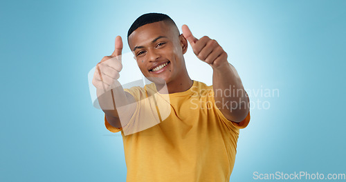 Image of Thumbs up, portrait and man in studio for success, winning deal and celebrate achievement on blue background. Happy model, emoji and like sign for feedback, voting yes and thank you for excellence
