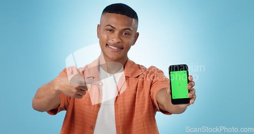 Image of Man, portrait and point at phone, green screen and review of mobile app, promotion or choice by blue background. Person, smartphone and happy with mockup space, chromakey or feedback for ui in studio