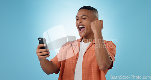 Image of Man, phone and fist with cheers in studio for trading profit, success or revenue by blue background. Investor, trader or person with smartphone for winning, prize or celebration with online giveaway