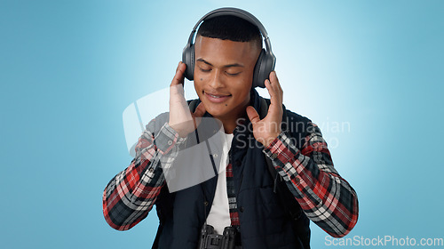 Image of Happy, man and headphones in studio for music, podcast and relax with audio subscription on blue background. Smile, freedom and young model listening to sound, streaming multimedia and hearing radio