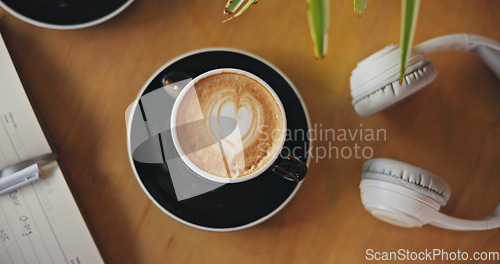 Image of Coffee, notebook and headphones on table, top view and breakfast for cappuccino, drink and matcha in diner. Cafe, restaurant and latte with heart, espresso and book with audio tech in morning in shop