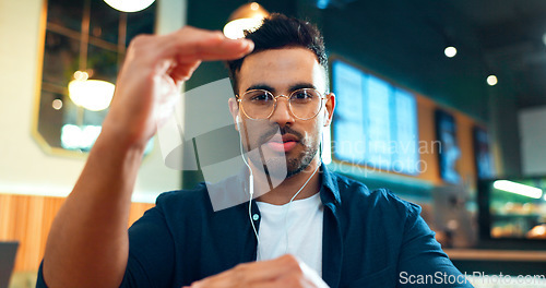 Image of Video call, portrait or man in cafe talking in mobile conversation as communication. Earphones, networking or entrepreneur in coffee shop or restaurant in discussion or speaking to explain online