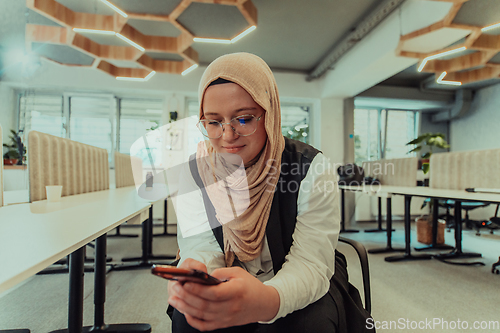 Image of A businesswoman in a hijab using a smartphone in a modern office, epitomizing a successful and empowered professional in today's tech-savvy world