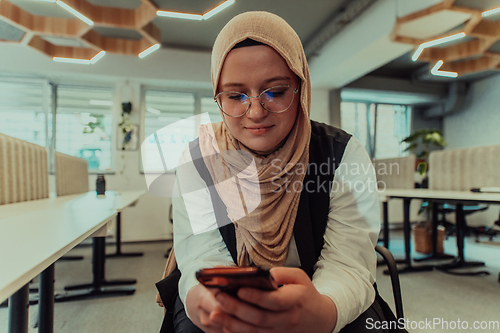 Image of A businesswoman in a hijab using a smartphone in a modern office, epitomizing a successful and empowered professional in today's tech-savvy world