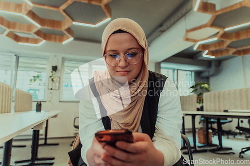 Image of A businesswoman in a hijab using a smartphone in a modern office, epitomizing a successful and empowered professional in today's tech-savvy world