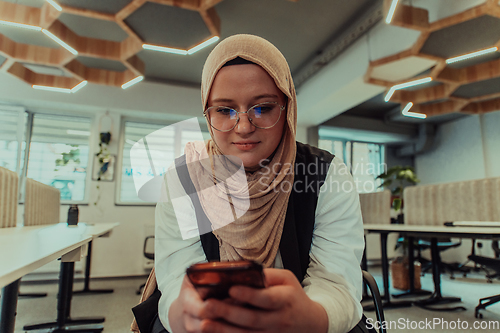 Image of A businesswoman in a hijab using a smartphone in a modern office, epitomizing a successful and empowered professional in today's tech-savvy world