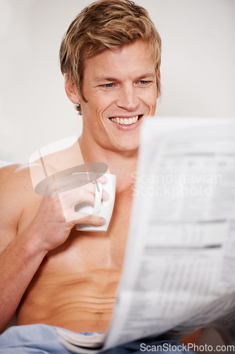 Image of Bed, coffee and a man reading the newspaper in his home to wake up in the morning after sleep or rest. Smile, tea and media with the body of a shirtless young person in the bedroom of an apartment