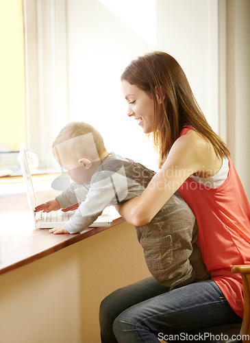 Image of Mother, holding and baby with laptop in home for remote, work or bond with child in kitchen. Young woman, parenting and son by smile for growth, milestone or development for care, love and support