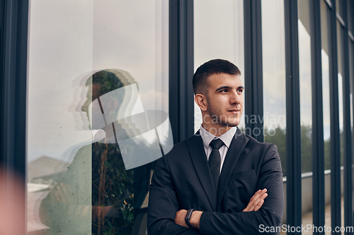 Image of A CEO dressed in a sleek black suit stands confidently at the entrance of a modern corporate building, awaiting the start of the workday in the bustling urban environment.