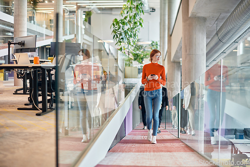 Image of In a vibrant modern startup office, a businesswoman with striking orange hair is immersed in her work at her desk, embodying the dynamic and creative spirit of contemporary entrepreneurship.