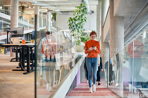 Image of In a vibrant modern startup office, a businesswoman with striking orange hair is immersed in her work at her desk, embodying the dynamic and creative spirit of contemporary entrepreneurship.