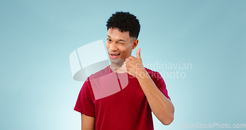 Image of Portrait, man and wink to call me in studio on blue background in communication mockup. Cape Town, male model and flirting with hand emoji for connection, cellular or network with contact in space