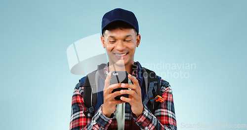 Image of Hiking, smile and typing with man, smartphone and internet on a blue studio background. Person, hiker and model with a cellphone, mobile user and contact with email, mockup space and website info