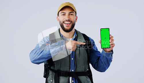 Image of Happy man, backpack and pointing to phone green screen on mockup or hiking app against a studio background. Portrait of male person or hiker smile and showing mobile smartphone display or travel tips