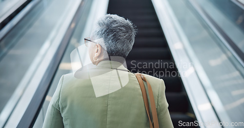 Image of Woman, back and travel on escalator in airport, building and thinking about work trip opportunity. Mature, businesswoman and walking with luggage and bag on stairs, steps or entrance in lobby