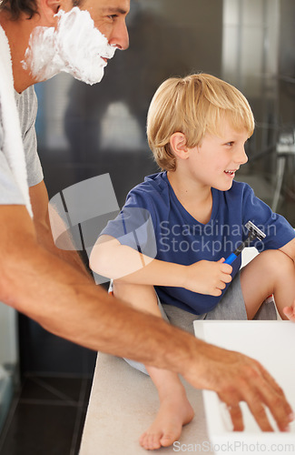 Image of Teaching him manly ways. A young boy sitting on the bathroom sink while his father shaves.