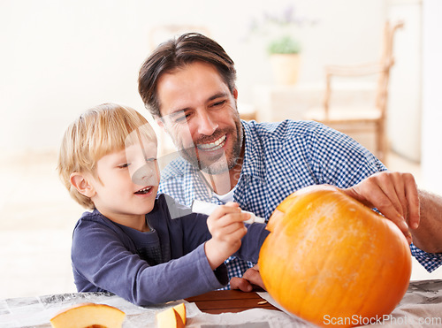 Image of Wait, one last thing. A father and son marking a pumpkin at home for halloween.