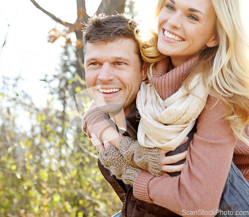 Image of Having fun in the Autumn sunshine. A happy man piggybacking his girlfriend while spending time in the woods.