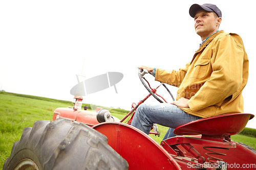 Image of Sitting in contemplation. A farmer sitting on his tractor and looking over a open field with copyspace.