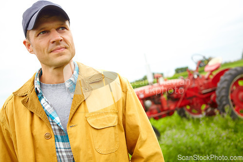 Image of Thinking aboyt ways to improve the farm. A farmer standing in a field with a tractor parked behind him - Copyspace.