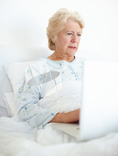 Image of Technology keeps her connected with her loved ones. Elderly female patient browses a laptop from her hospital bed.