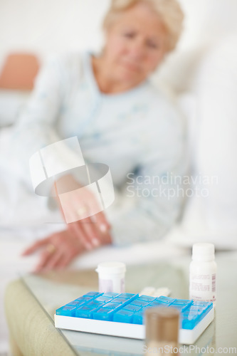 Image of Daily dosage - Senior Health. Closeup of a daily medical dosage with woman reaching for it blurred in background.