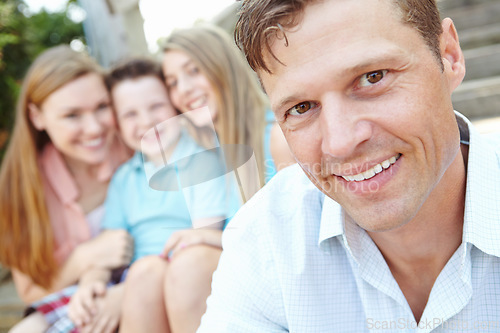 Image of Portrait of a perfect family. Handsome father with family sitting behind him while outdoors.