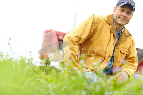 Image of Enjoying the fresh farm air. Portrait of a farmer kneeling in a field with his tractor parked behind him.