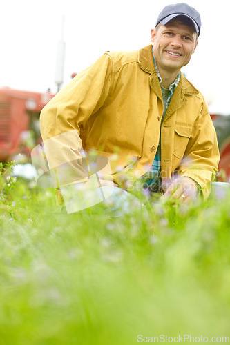 Image of Hes a happy and confident farmer. Portrait of a farmer kneeling in a field with his tractor parked behind him.