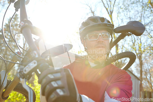 Image of Deciding which way to go next...Closeup of a male cyclist wearing glasses, a helmet and gloves while carrying his bicycle through the woods. Mature sportsman out cycling in nature on a sunny day.