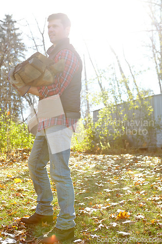 Image of One male lumberjack holding wooden logs after chopping tree in remote landscape. Serious focused adult man in autumn wear standing alone outside, carrying firewood from the forest