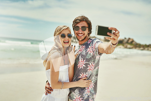 Image of Guess whos engaged. an affectionate young couple taking selfies after their engagement on the beach.
