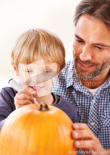 Image of Ill carve it after you mark out the face. A father and son marking a pumpkin in the kitchen for halloween.