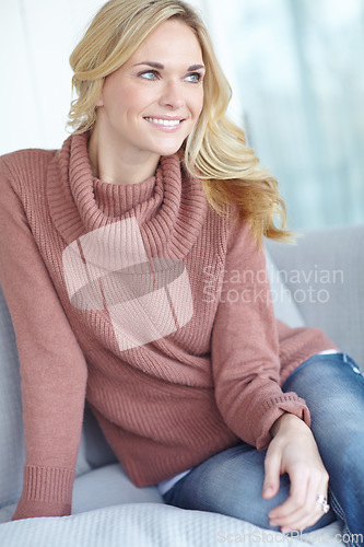 Image of Woman sitting on couch at home alone looking away. Beautiful female smiling on her sofa relaxed and calm on lovely day. Happy attractive lady enjoying her comfortable apartment