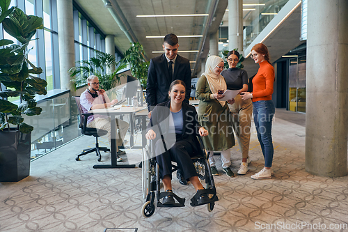 Image of A diverse group of business colleagues is having fun with their wheelchair-using colleague, demonstrating their attention and inclusivity in the workplace