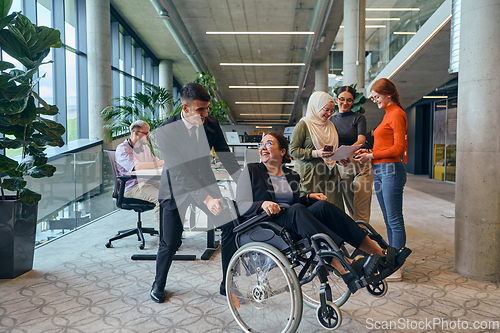 Image of A diverse group of business colleagues is having fun with their wheelchair-using colleague, demonstrating their attention and inclusivity in the workplace