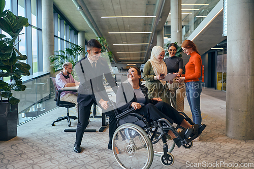 Image of A diverse group of business colleagues is having fun with their wheelchair-using colleague, demonstrating their attention and inclusivity in the workplace