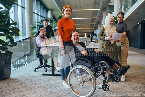 Image of A diverse group of business colleagues is having fun with their wheelchair-using colleague, demonstrating their attention and inclusivity in the workplace